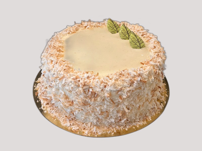 Whole banana coconut cake covered in toasted coconut flakes with pale green chocolate leaves on top