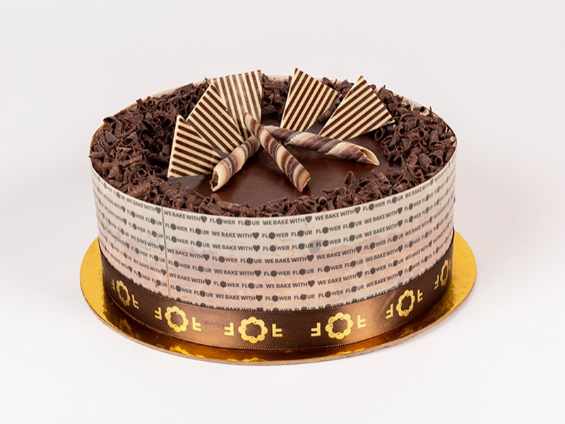 Flower Flour chocolate cake topped with chocolate curls and striped chocolate fans, wrapped in a Flower Flour band
