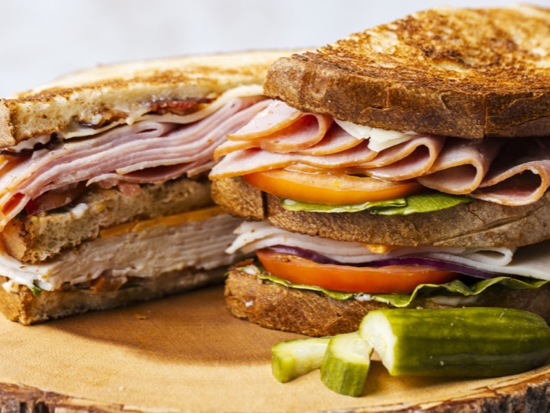 A club sandwich stacked with turkey and ham on a wooden board