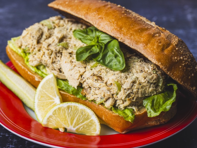 A tuna sandwich on a toasted roll with basil
