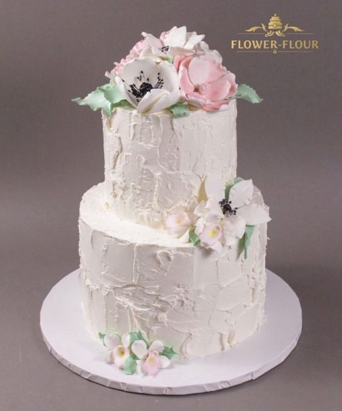 A two-tier textured white buttercream cake with white and pink sugar flowers