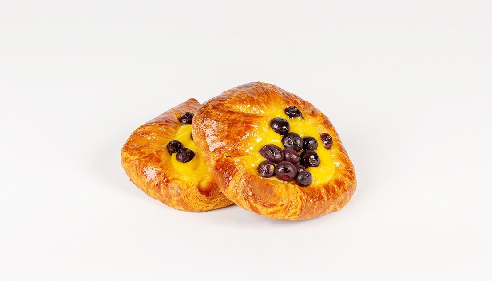 Two glazed pastries filled with yellow custard and topped with blueberries