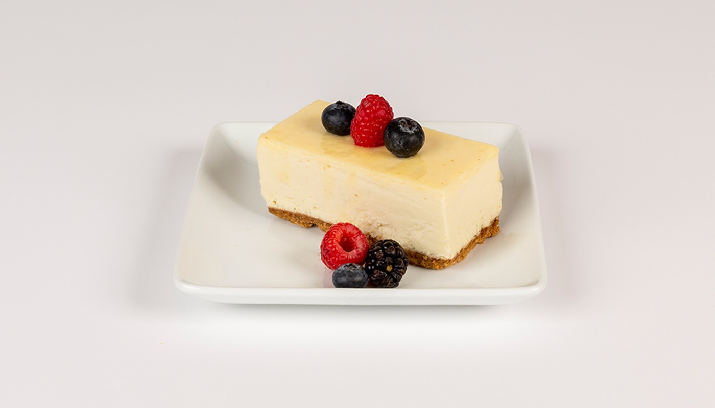 A slice of cheesecake with a graham crust, topped with raspberries and blueberries