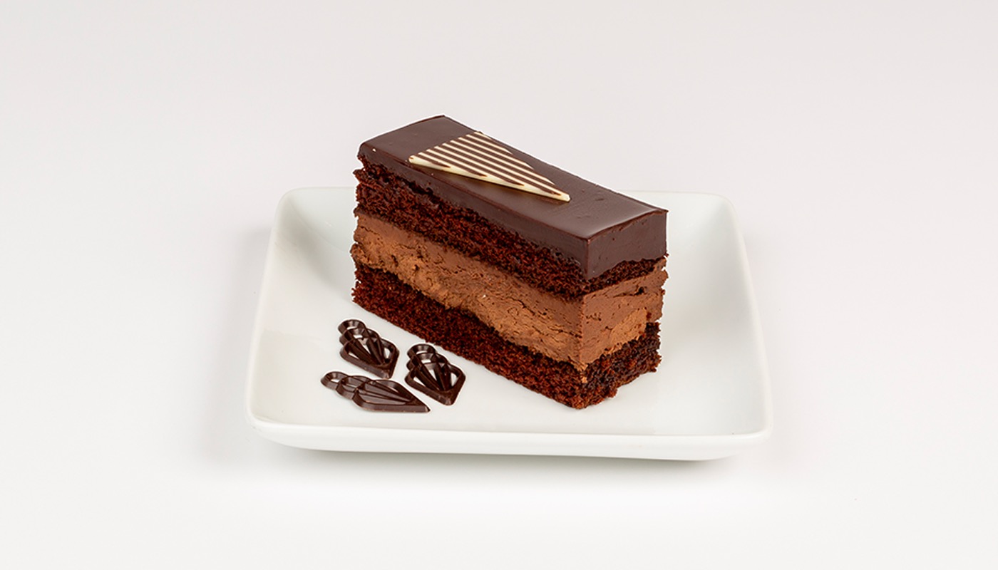 A slice of layered chocolate cake with chocolate mousse and a glossy ganache top, on a white plate