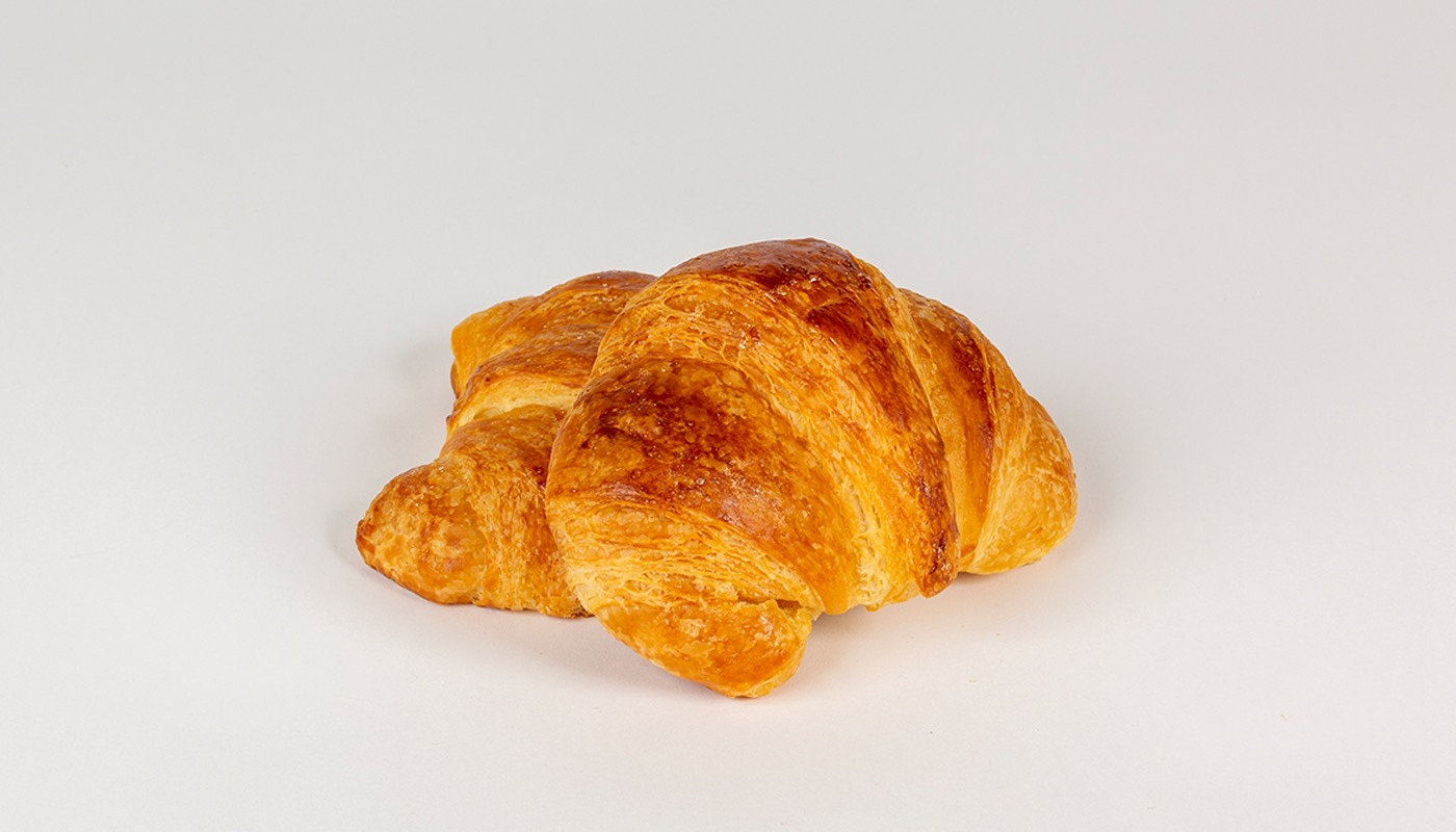 A golden, flaky plain croissant on a white background