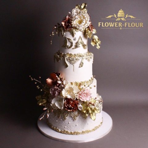 A four-tier white wedding cake with gold lace and sugar peonies